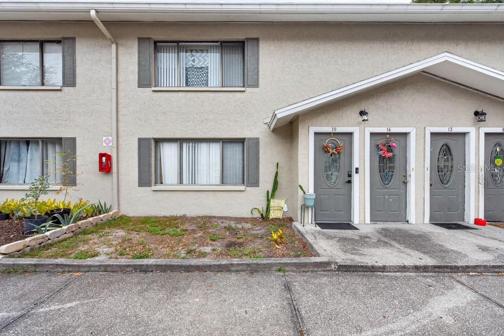 The exterior of a two-story apartment building features gray doors, windows with shutters, and landscaping — 1409 ALPINE ROAD UNIT 10, CLEARWATER, FL