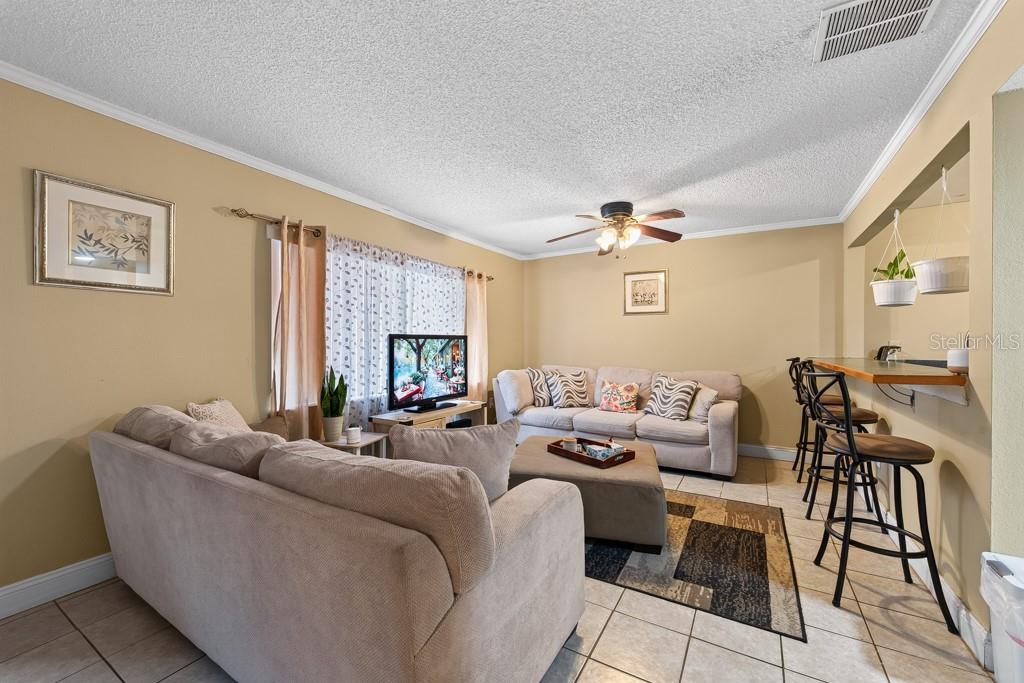 A living room with beige sofas, a television, a ceiling fan, and a breakfast bar — 1409 ALPINE ROAD UNIT 10, CLEARWATER, FL