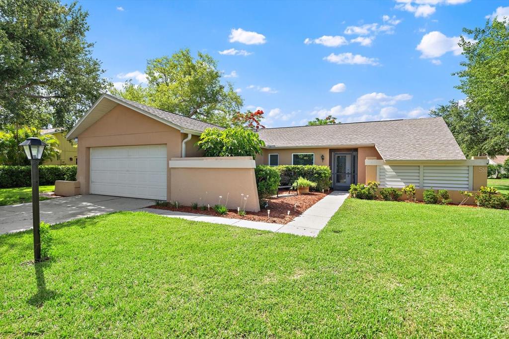 A single-story house with a tan stucco exterior, a two-car garage, and a front lawn — 4352 KINGSTON LOOP, SARASOTA, FL