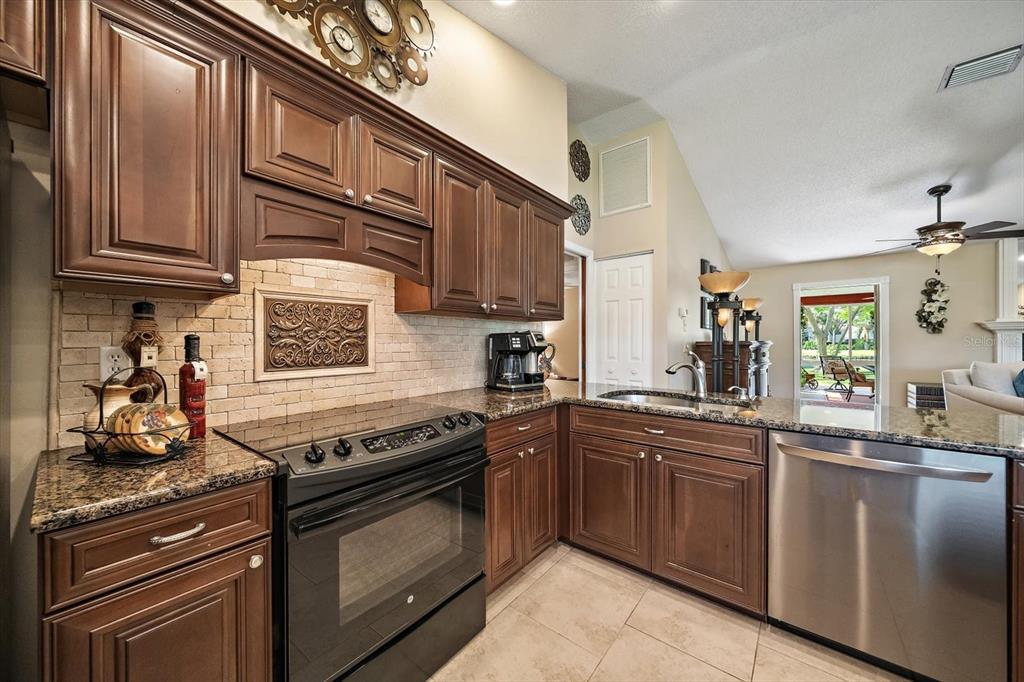 A kitchen features dark wood cabinets, granite countertops, stainless steel appliances, and a tiled backsplash — 4352 KINGSTON LOOP, SARASOTA, FL