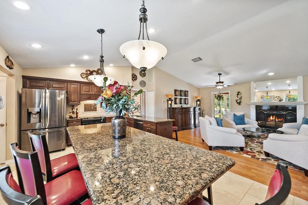 A kitchen with a granite island and red chairs opens into a living room area — 4352 KINGSTON LOOP, SARASOTA, FL