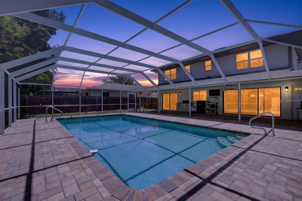 A rectangular swimming pool with a screen enclosure sits on a paved patio at dusk — 2178 MARQUITA DRIVE, DUNEDIN, FL