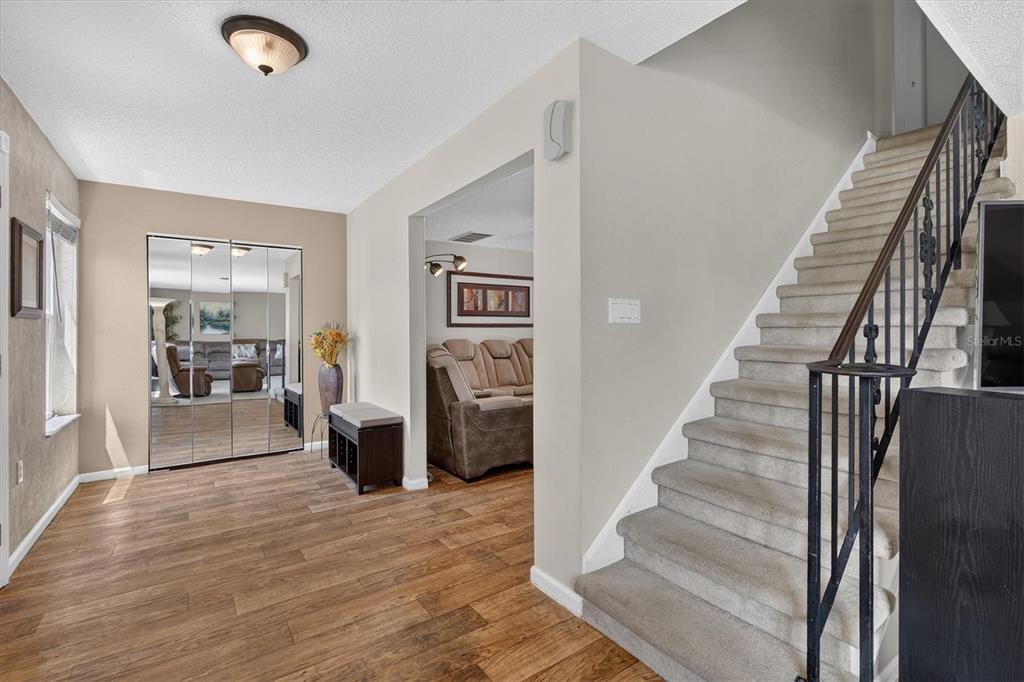 A foyer with wood-look flooring, mirrored closet doors, and a carpeted staircase with metal railings — 2178 MARQUITA DRIVE, DUNEDIN, FL