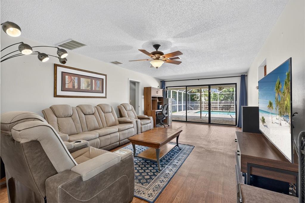 A living room features a beige sectional sofa, wood flooring, a ceiling fan, and pool views — 2178 MARQUITA DRIVE, DUNEDIN, FL