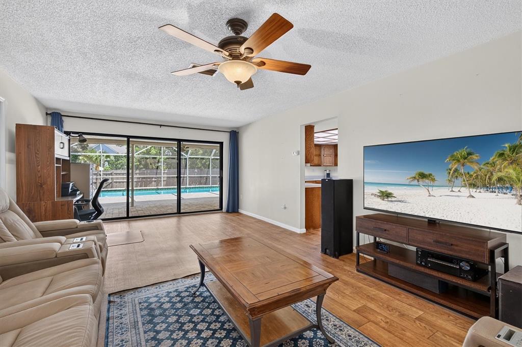 A living room features a ceiling fan, wood flooring, a large television, and sliding glass doors — 2178 MARQUITA DRIVE, DUNEDIN, FL