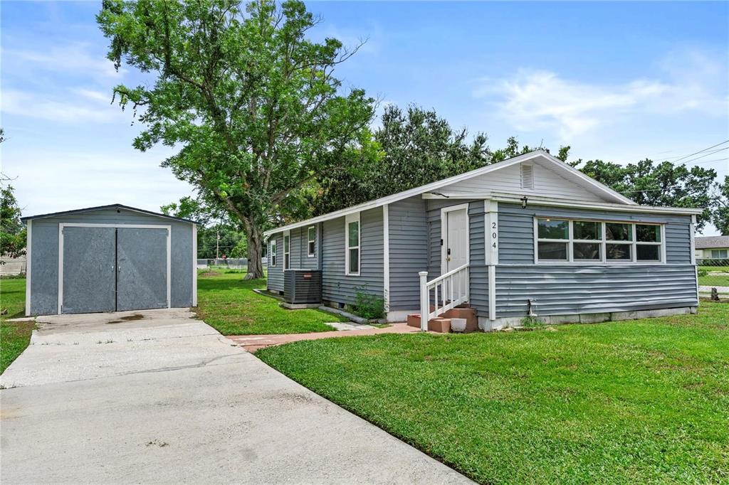A gray single-story house with a detached garage and a concrete driveway on a lawn — 204 PINE AVENUE, POLK CITY, FL