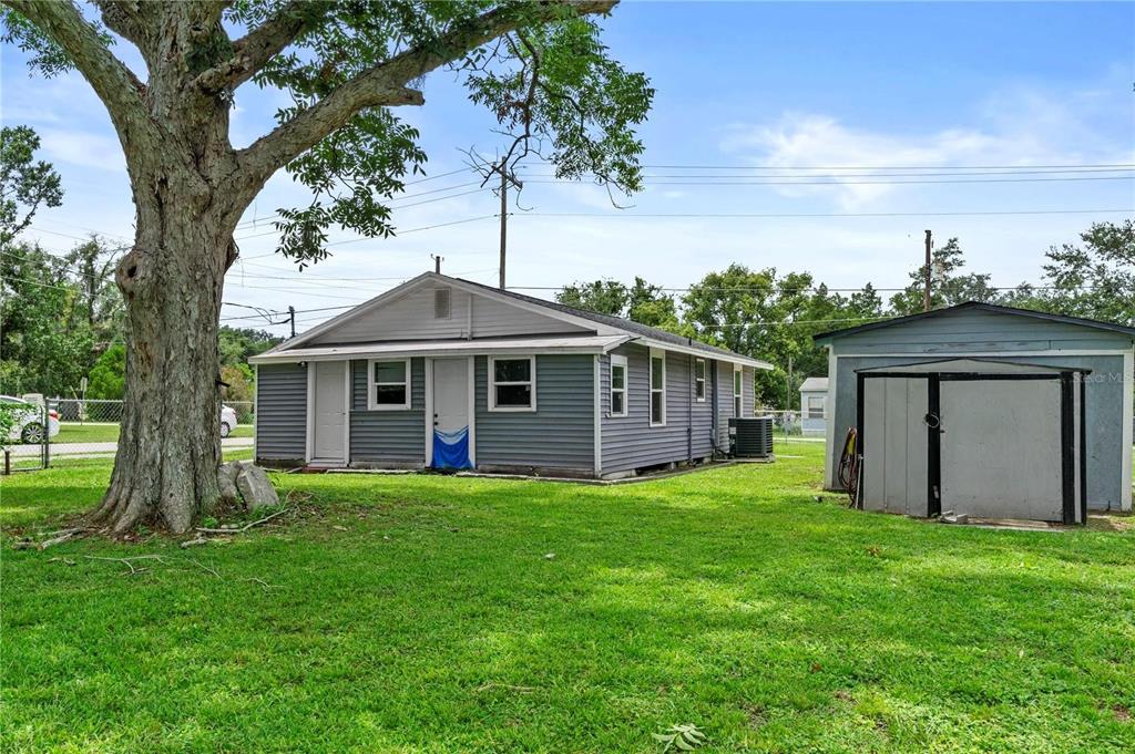 A gray, single-story house with a detached shed sits on a grassy lot with trees — 204 PINE AVENUE, POLK CITY, FL