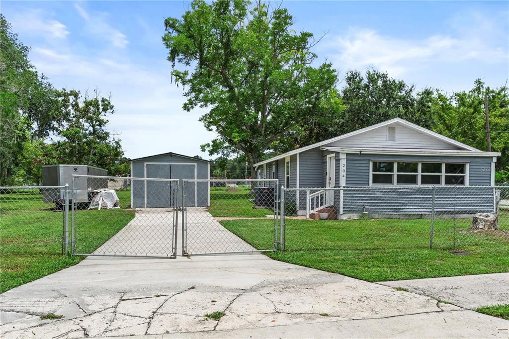 A gray house with a detached shed and a fenced yard sits behind a concrete driveway — 204 PINE AVENUE, POLK CITY, FL
