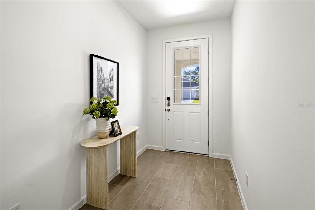 A bright entryway features a white front door, a wood console table, and tiled flooring — 141 GREENHOUSE GROVE STREET, GROVELAND, FL