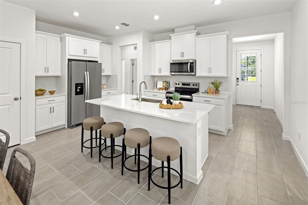 A modern kitchen features white cabinetry, a central island with bar seating, and tile flooring — 141 GREENHOUSE GROVE STREET, GROVELAND, FL