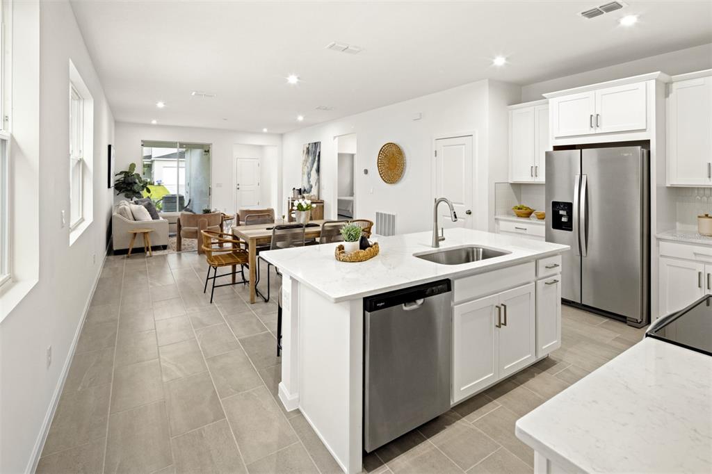 A modern kitchen with white cabinets, a quartz island, and stainless steel appliances overlooks a dining area — 141 GREENHOUSE GROVE STREET, GROVELAND, FL