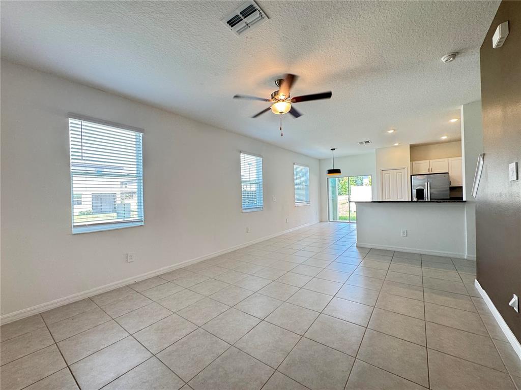 An open-concept living area features light-colored tile flooring, white walls, and a kitchen with appliances — 10268 HONEY HAMMOCK WAY, SAN ANTONIO, FL