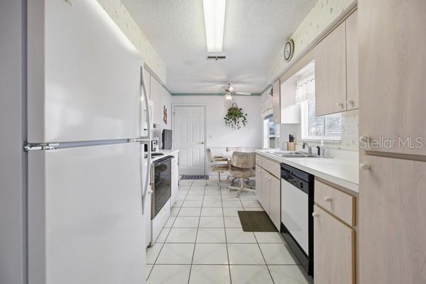 A galley kitchen features light-colored cabinets, white appliances, and a tiled floor leading to a dining area — 17831 SE 96TH AVENUE, SUMMERFIELD, FL