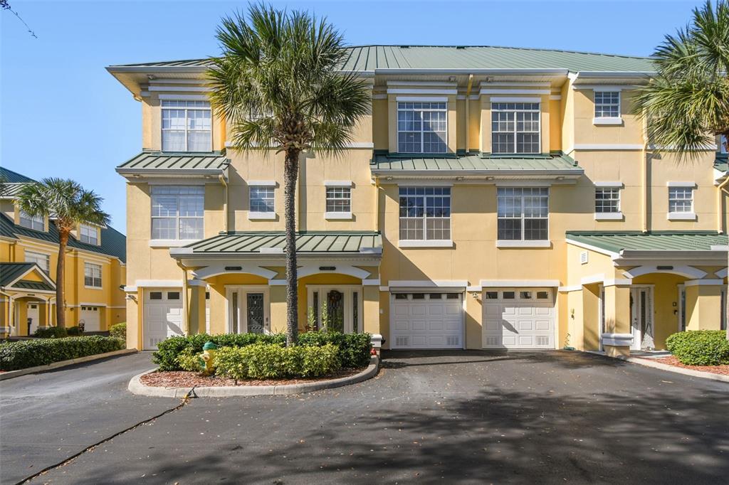 A three-story yellow townhouse with a green metal roof and attached garages — 6331 SUNSET BAY CIRCLE, APOLLO BEACH, FL