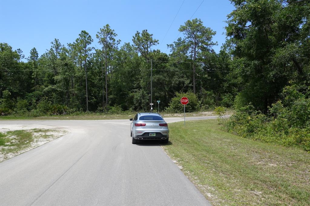 A silver car is parked on a paved road near a stop sign and woods — SW 38th Street & SW 159 COURT, OCALA, FL