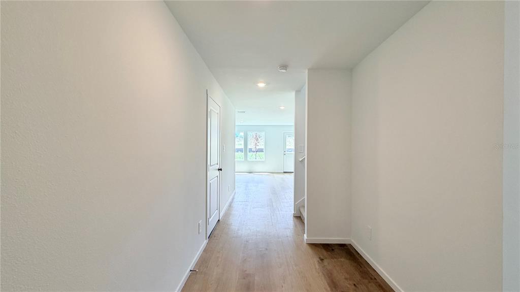 A bright hallway with light wood-look flooring leads toward a living area with large windows — 583 ARTEMIS STREET, LAKE WALES, FL