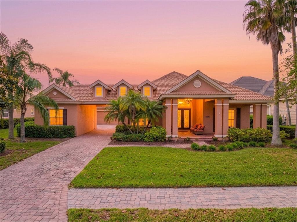 A single-story stucco house with a tiled roof, brick driveway, and palm trees at sunset — 4714 MAINSAIL DRIVE, BRADENTON, FL