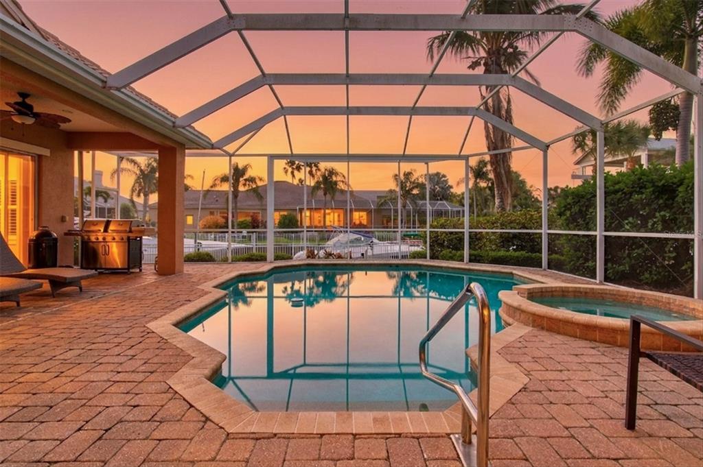 A screened-in patio features a swimming pool, a hot tub, and brick pavers at sunset — 4714 MAINSAIL DRIVE, BRADENTON, FL