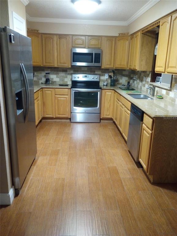 A kitchen with light wood cabinets, stainless steel appliances, granite countertops, and wood-look tile flooring — 13300 NE 38TH AVENUE, ANTHONY, FL