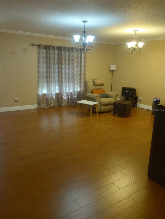 A living room with wood-look tile flooring, two chandeliers, and a recliner near a window — 13300 NE 38TH AVENUE, ANTHONY, FL