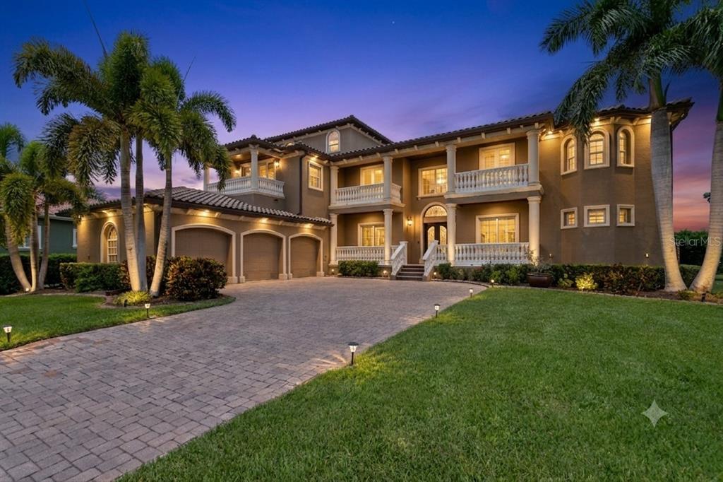 A large two-story Mediterranean-style house with a three-car garage and a paved driveway at dusk — 6459 RUBIA CIRCLE, APOLLO BEACH, FL