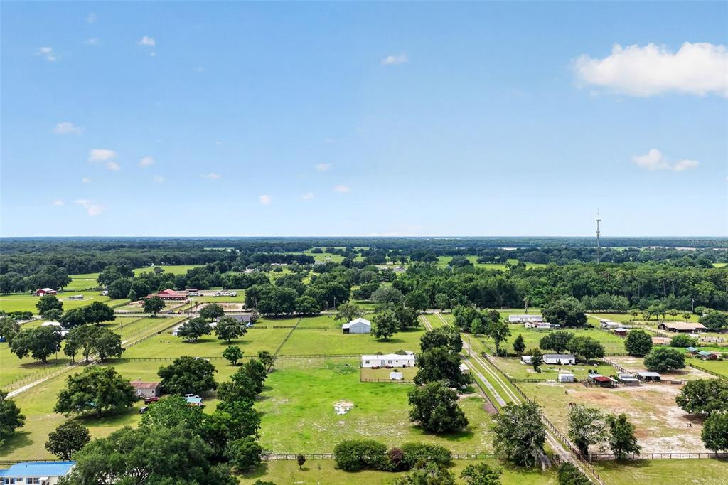 An aerial view shows a rural landscape with green pastures, scattered trees, and several buildings — 311 SE HIGHWAY 42, SUMMERFIELD, FL