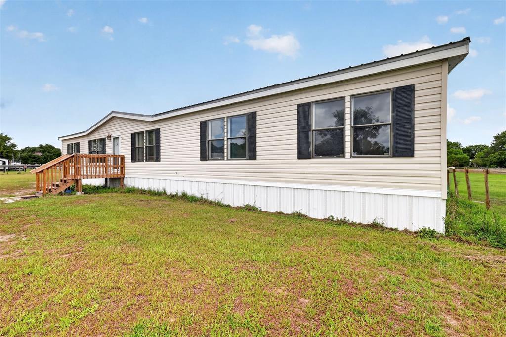 A single-story manufactured home with beige siding and a wooden deck sits on a lawn — 311 SE HIGHWAY 42, SUMMERFIELD, FL