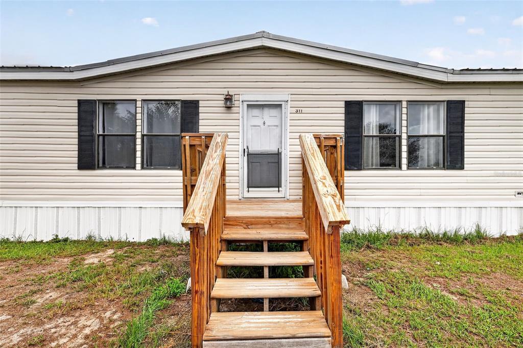 A single-story manufactured home with light siding, black shutters, and a wooden front staircase — 311 SE HIGHWAY 42, SUMMERFIELD, FL