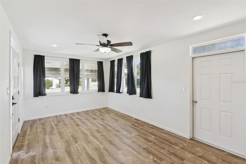 A bright living room features white walls, wood-look flooring, a ceiling fan, and black curtains — 822 POINSETTIA DRIVE, EUSTIS, FL