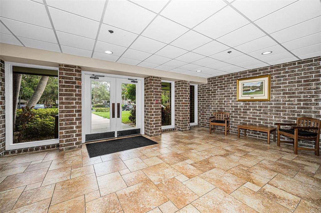 A lobby with a brick wall, tile flooring, drop ceiling, and double glass entry doors — 36750 US HIGHWAY 19 N UNIT 20-209, PALM HARBOR, FL