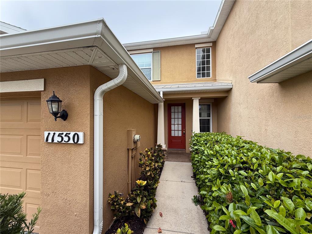 The exterior of a tan stucco house features a red front door and a walkway — 11550 52ND COURT E, PARRISH, FL