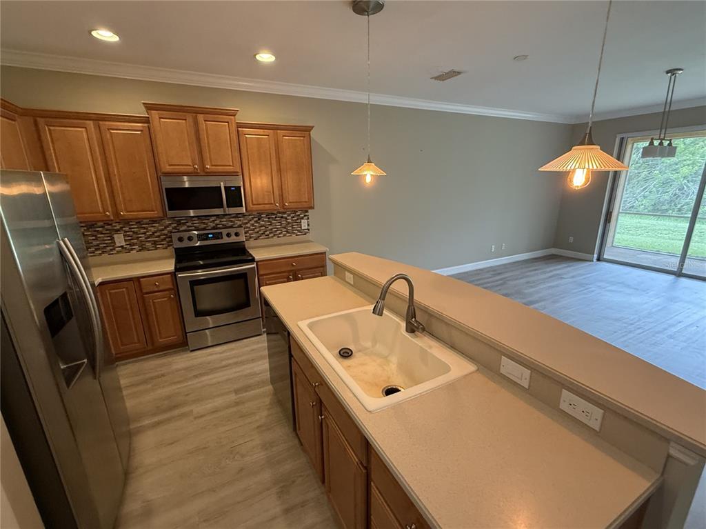 A kitchen with wood cabinets, stainless steel appliances, and a sink island overlooks a living area — 11550 52ND COURT E, PARRISH, FL