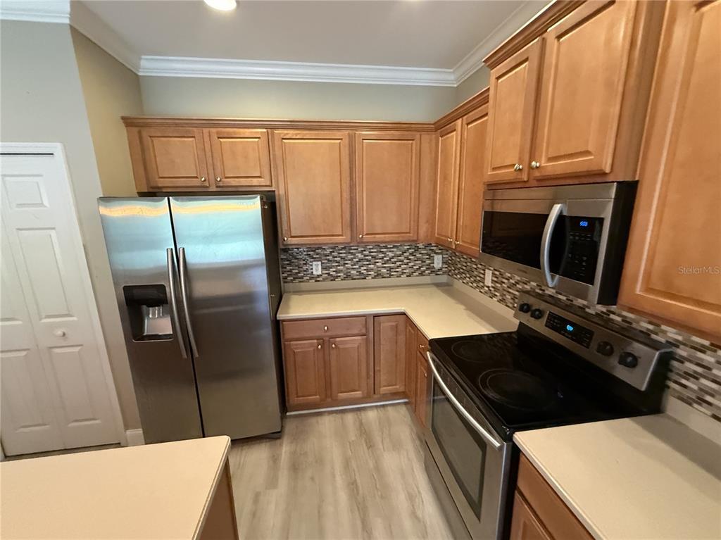 A kitchen features wood cabinets, stainless steel appliances, a mosaic tile backsplash, and light flooring — 11550 52ND COURT E, PARRISH, FL