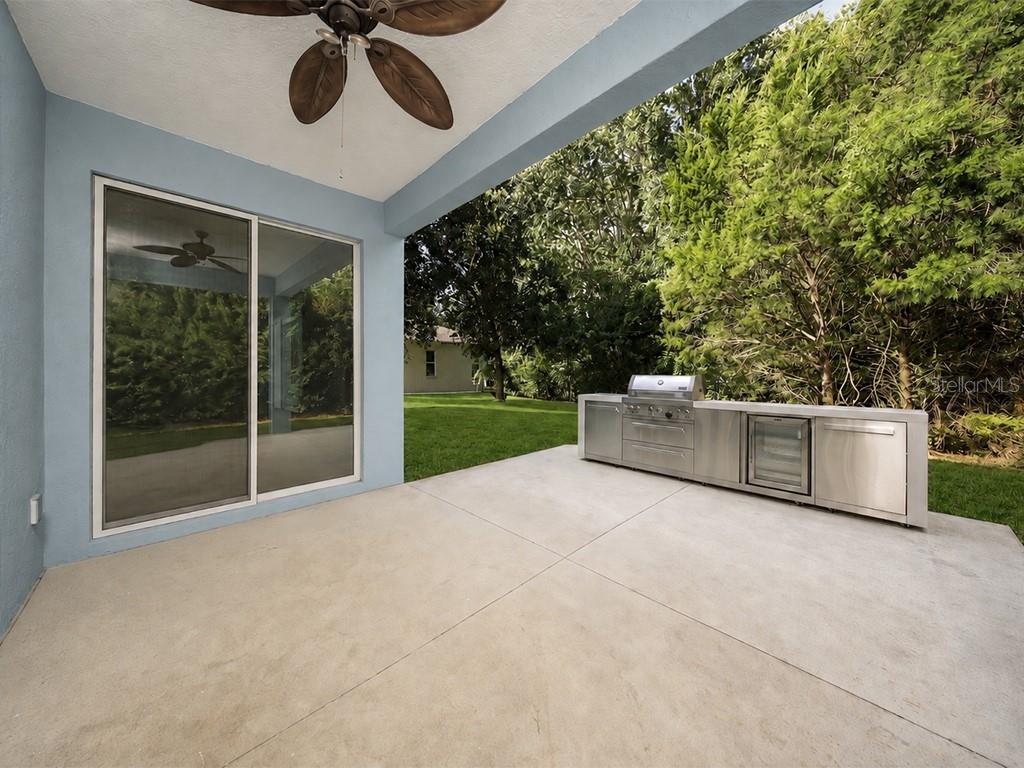 A covered patio features a concrete floor, a ceiling fan, and a stainless steel outdoor kitchen — 8710 PRESTON WOODS COURT, LAND O LAKES, FL