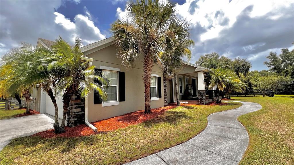 A single-story house with a curved concrete walkway, palm trees, and red mulch landscaping — 3060 RAMBLER AVENUE, ST CLOUD, FL