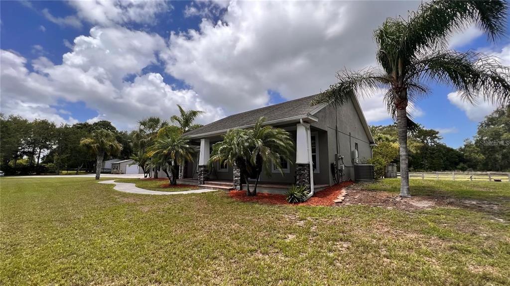 A single-story house with a covered porch, stone pillars, and palm trees in the yard — 3060 RAMBLER AVENUE, ST CLOUD, FL