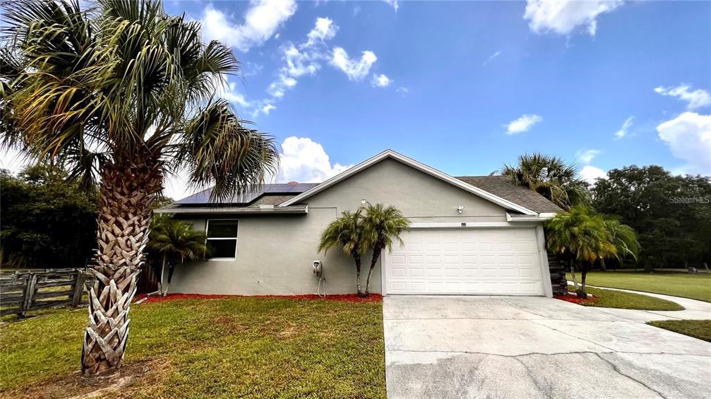 A single-story house with a two-car garage, solar panels, and palm trees in the yard — 3060 RAMBLER AVENUE, ST CLOUD, FL