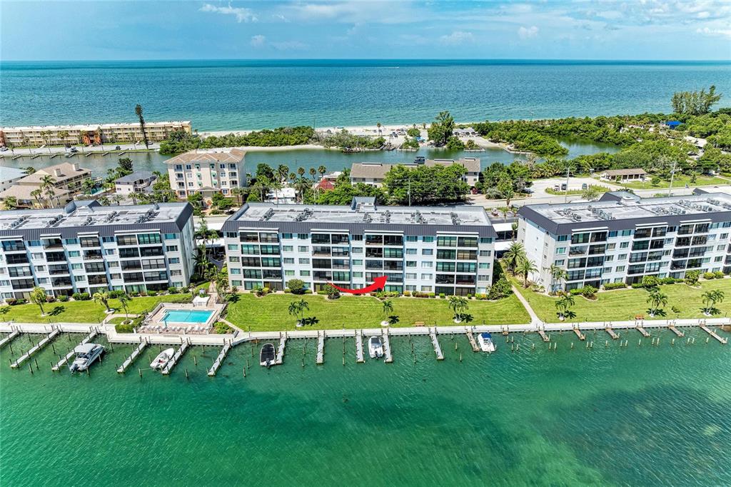 An aerial view of a multi-story waterfront condominium complex with a boat dock and pool — 8977 MIDNIGHT PASS ROAD UNIT 219, SARASOTA, FL