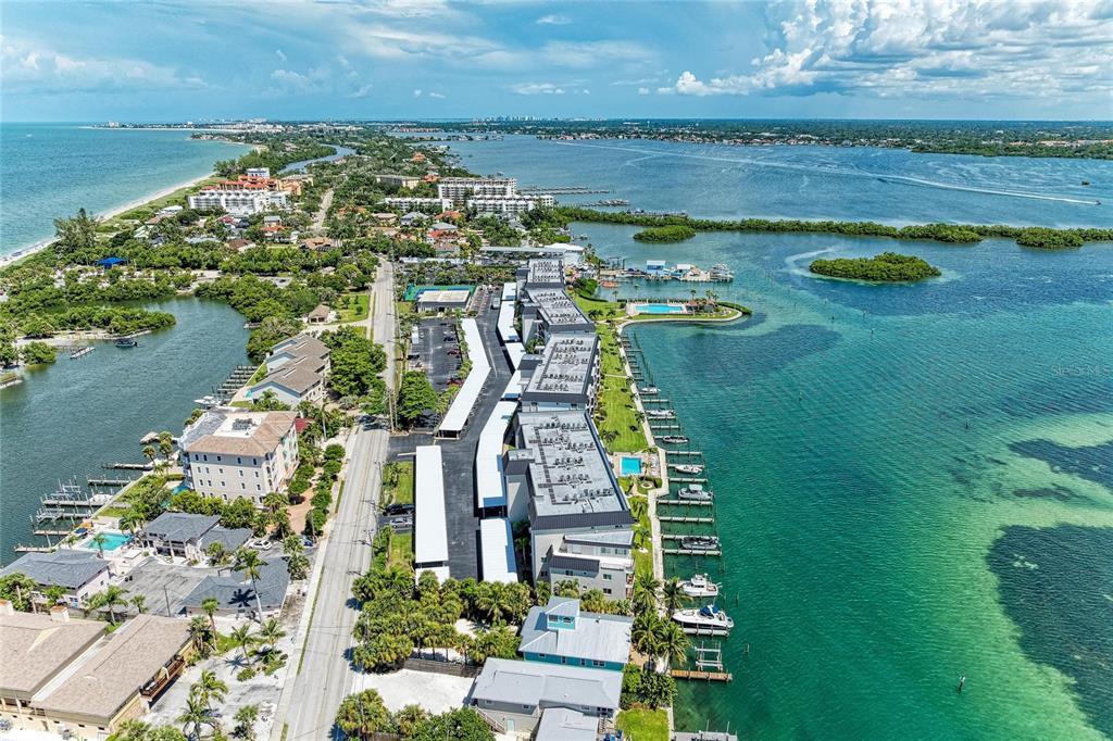 An aerial view shows a coastal residential complex with a marina, parking, and surrounding water — 8977 MIDNIGHT PASS ROAD UNIT 219, SARASOTA, FL