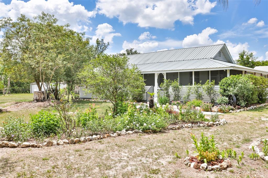 A light-colored house with a metal roof and a front porch sits behind a garden — 610 LYLE PARKWAY, BARTOW, FL