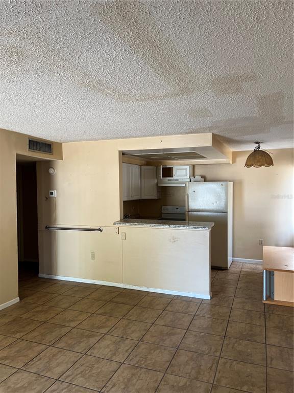 A kitchen with white cabinets and a refrigerator is visible from an adjacent tiled room — 800 N FISKE BOULEVARD UNIT 606, COCOA, FL