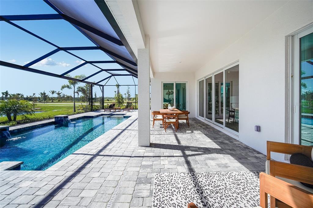 A covered patio features a swimming pool, dining set, and sliding glass doors to the home — 20009 TROUT TERRACE, LAKEWOOD RANCH, FL