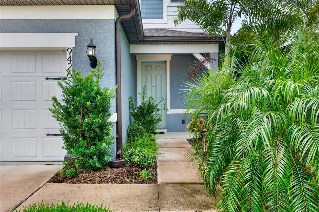 A light blue house exterior features a garage, a front door, and lush landscaping — 9426 LAMINE WAY, PARRISH, FL
