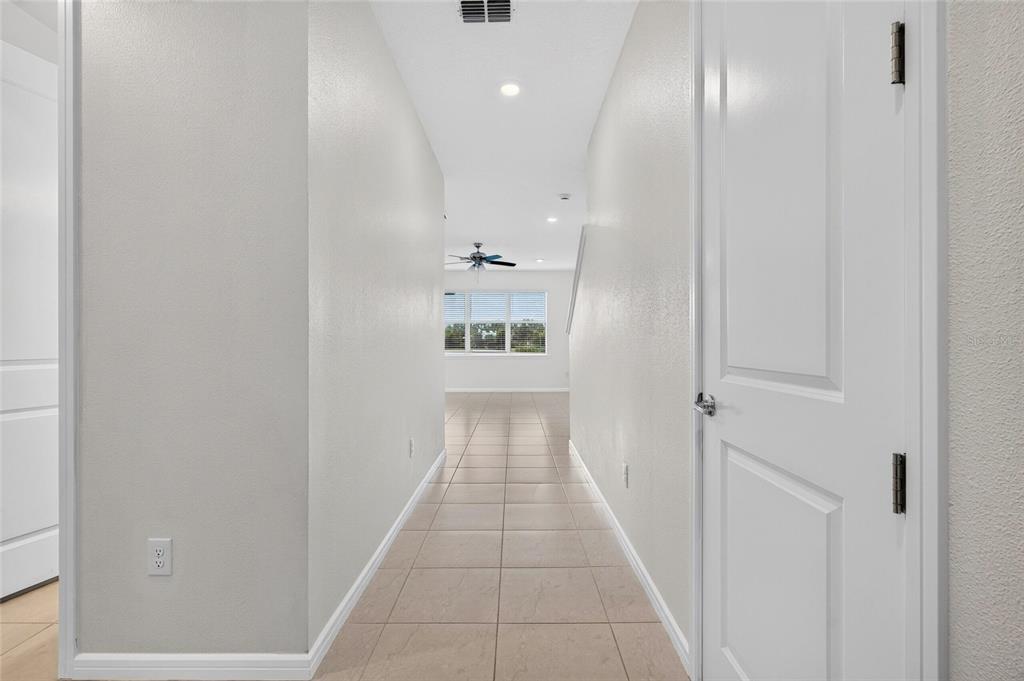A tiled hallway leads toward a bright living area with a ceiling fan and windows — 9426 LAMINE WAY, PARRISH, FL