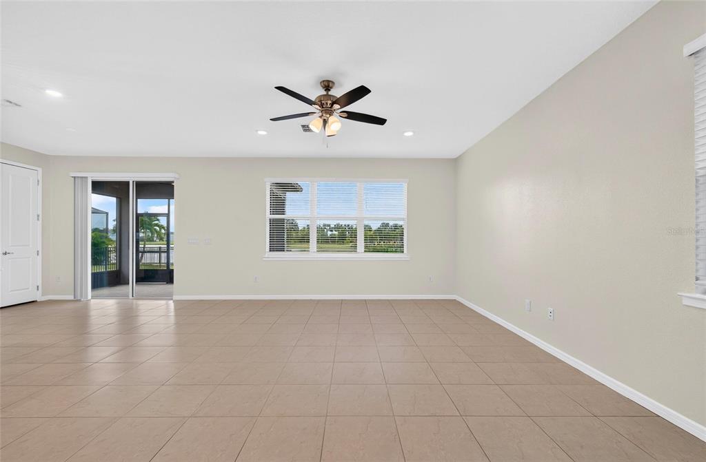 A spacious, empty living room features beige tile flooring, a ceiling fan, and sliding glass doors — 9426 LAMINE WAY, PARRISH, FL