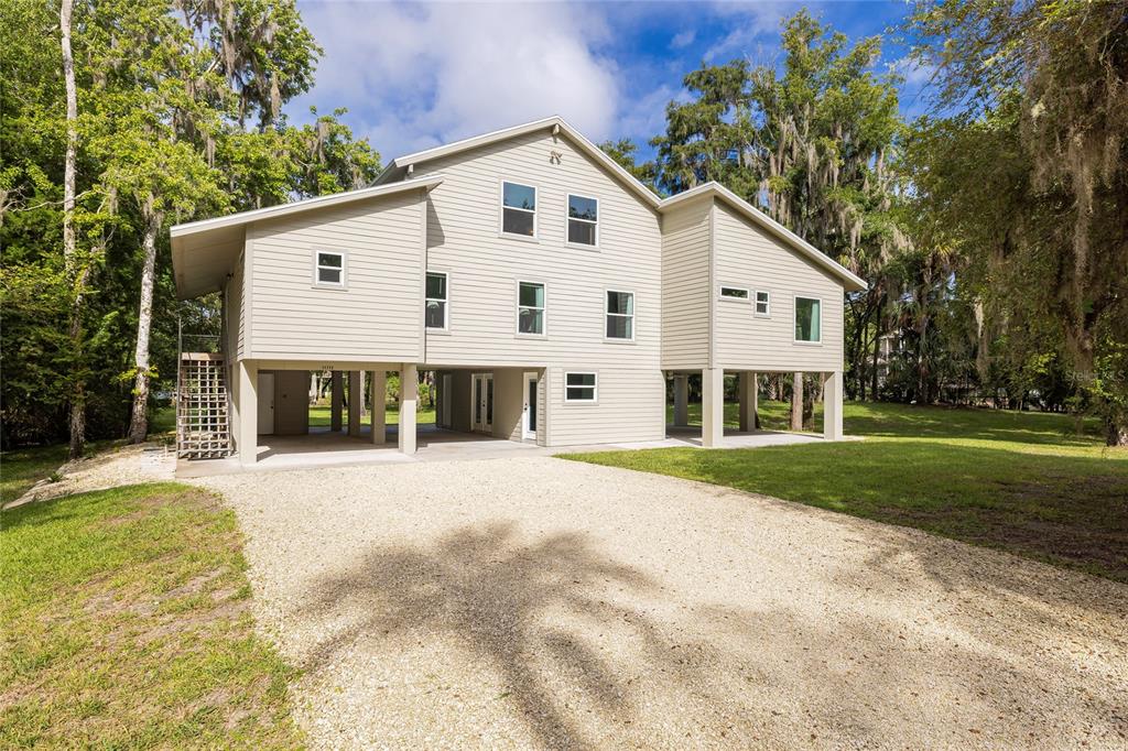 A two-story house on stilts with light-colored siding and a gravel driveway — 11772 N RIVER SOUND PATH, INGLIS, FL