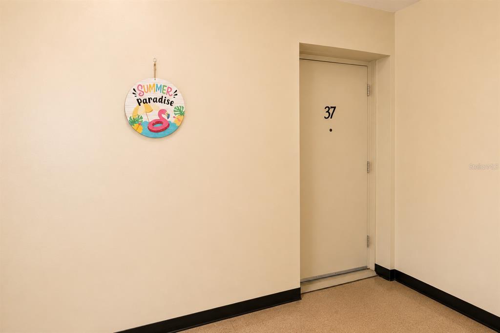 A beige hallway features a door labeled 37 and a circular summer-themed wall decoration — 2459 FRANCISCAN DRIVE UNIT 37, CLEARWATER, FL