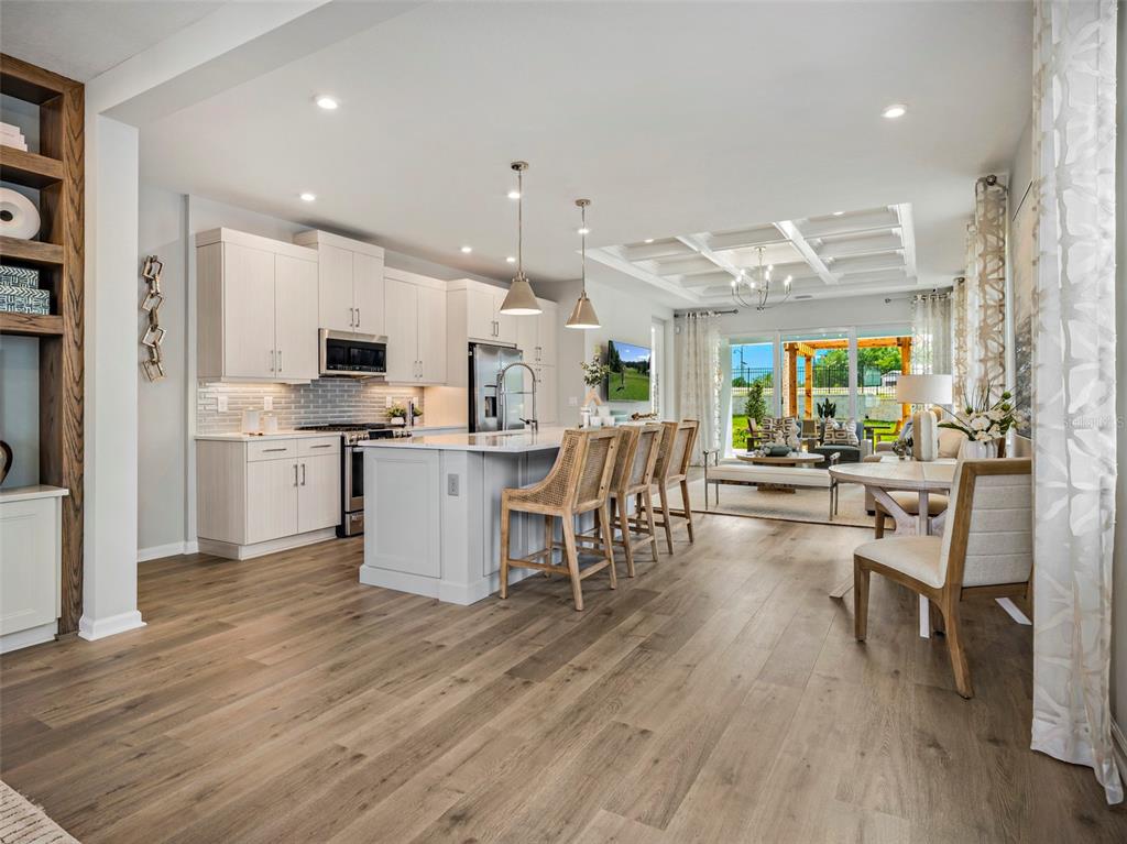A modern kitchen with light wood cabinets, a central island, and an open living area — 419 VERONA WAY, LADY LAKE, FL