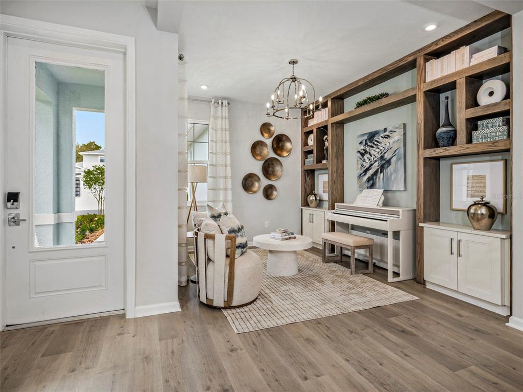 A bright living room features a white piano, built-in wooden shelving, and a circular armchair — 419 VERONA WAY, LADY LAKE, FL