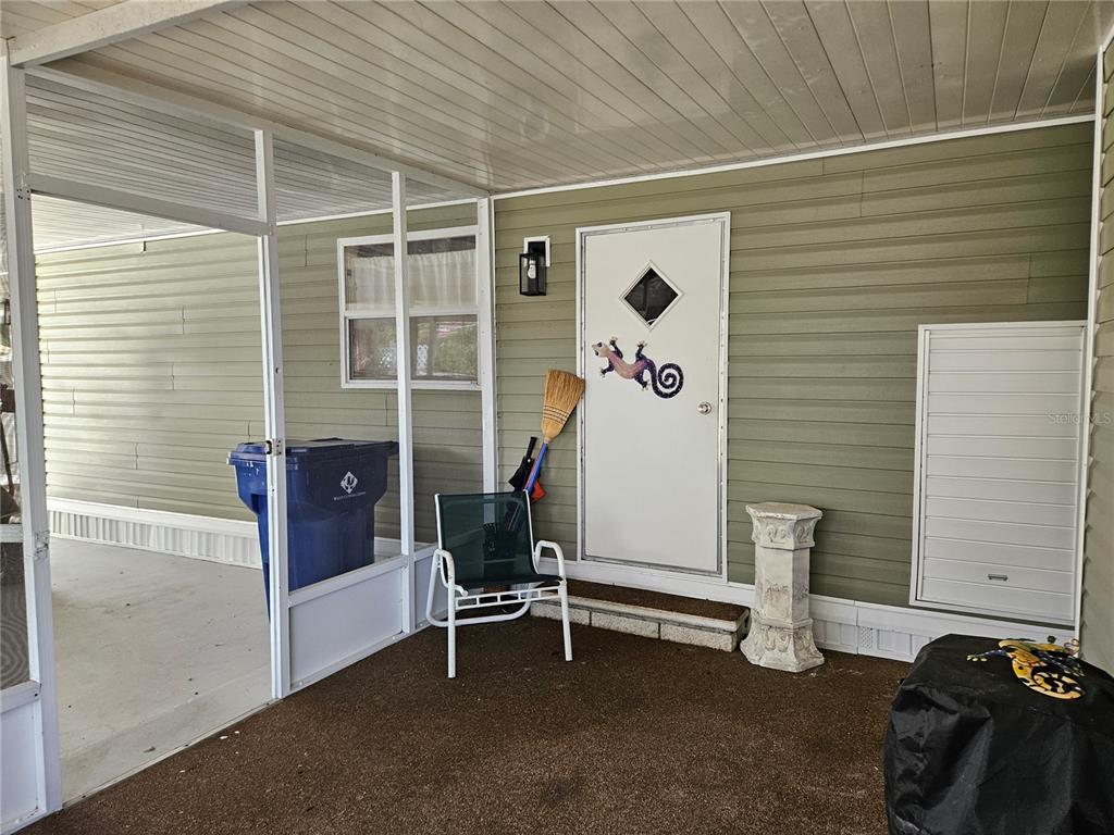 A covered porch features green siding, a white door, a chair, and a blue bin — 217 LAKE TARPON DRIVE UNIT 24, PALM HARBOR, FL